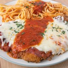 chicken parmesan with sauce and noodles on a white plate sitting on a wooden table