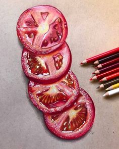 some pencils are laying on the table next to tomatoes and one is cut in half