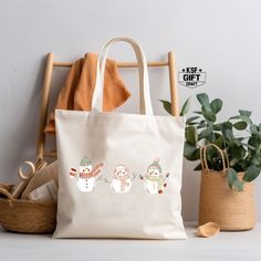 a white tote bag with three snowmen on it next to a potted plant