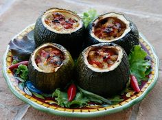 four stuffed vegetables on a plate with lettuce and chilis in the center