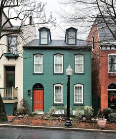 a row of houses with red doors and windows on the side of each house, in front of a street lamp