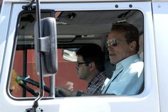 two men sitting in the driver's seat of a truck looking out the window