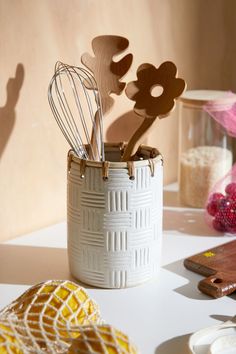 a white vase filled with kitchen utensils on top of a table