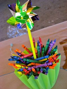 a vase filled with lots of crayons sitting on top of a table next to a pinwheel