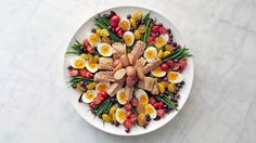 a white plate topped with eggs, meat and veggies on top of a marble table