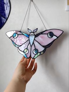 a hand holding a stained glass butterfly hanging from a chain on a wall next to a mirror