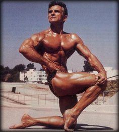 a bodybuilding man posing for the camera with his hands on his hips and legs crossed