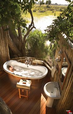 an outdoor bathroom with a tub, sink and toilet in the middle of wood planked flooring