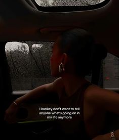 a woman sitting in the back seat of a car with rain falling on her windshield