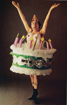 a woman holding a giant cake with candles on it's face and hands in the air