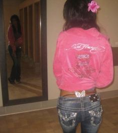 a girl in jeans and a pink shirt is looking at her reflection in the mirror