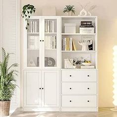 a white bookcase filled with books next to a potted plant