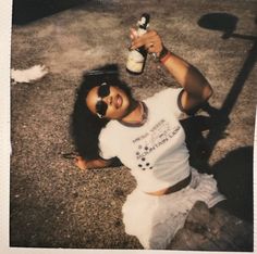 a man in white shirt and skirt sitting on the ground with beer bottle next to him