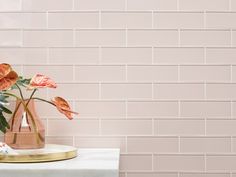 two vases with flowers on a table in front of a pink brick wall background