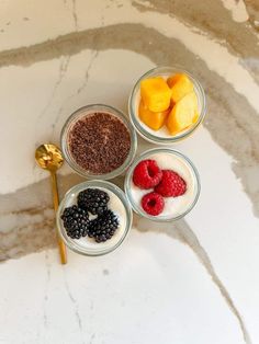 four small glass bowls filled with different types of fruit and yogurt on a marble counter top