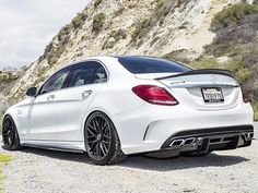 the rear end of a white mercedes c - class coupe parked in front of a mountain