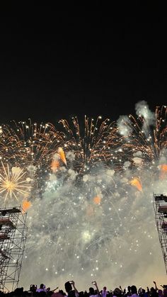 fireworks are lit up in the night sky with people standing on stage to watch them