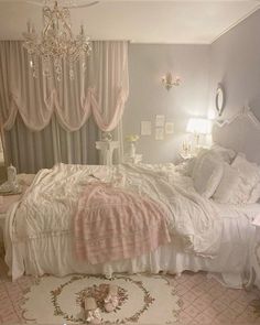 a white bed sitting in a bedroom next to a chandelier and window covered with curtains