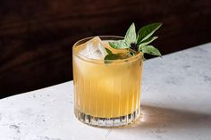 a close up of a drink on a table with ice and green leafy garnish