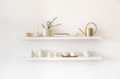 two white shelves with cups and vases on them