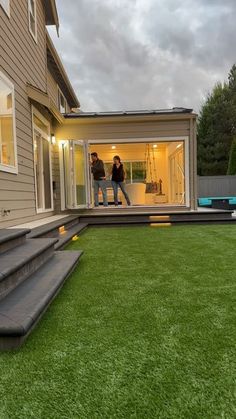 two people are standing in the back door of a house with stairs leading up to it