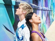 two people standing in front of a wall with graffiti on it and one person wearing ear buds