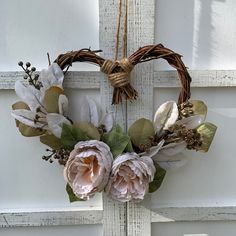 a wreath hanging on the front door with two flowers and leaves in it, attached to a cross