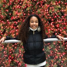 a woman standing in front of a christmas tree with her hands on the railings