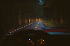 the dashboard of a car driving down a road in the woods at night with lights on