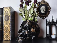 a black skull vase with flowers in it next to two books and a candle holder