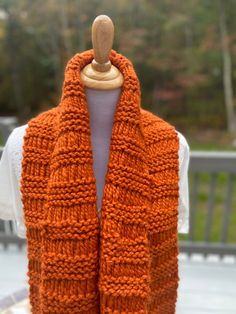 an orange knitted scarf hanging on a mannequin's dummy with trees in the background