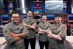 four people standing in front of a tv set with their arms crossed and looking at the camera