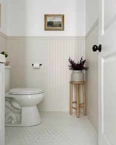 a white toilet sitting in a bathroom next to a wooden stool with flowers on it