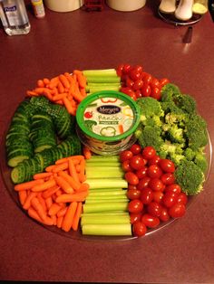 a platter filled with lots of vegetables on top of a table next to a container of yogurt