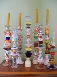 a collection of glass vases and candles on a wooden table in front of a wall