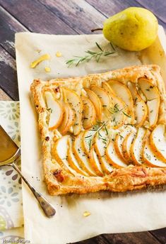 an apple tart with sliced pears and rosemary on top next to a spoon