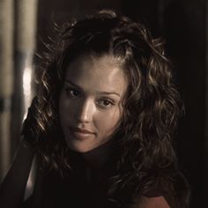 a woman with long curly hair is looking at the camera and has her hand on her head