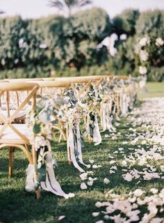 rows of wooden chairs lined up with flowers and ribbons on the grass at an outdoor ceremony