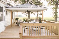 a wooden deck with chairs and table under a gazebo next to a white house