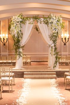 an indoor wedding ceremony with white flowers and petals on the aisle leading up to the altar