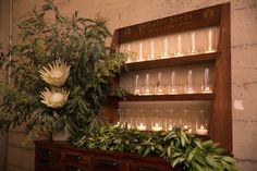 flowers and candles are on display in front of a shelf with wine glasses filled with water