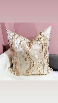 a white and gold pillow sitting on top of a fur covered floor next to a pink wall