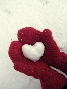 a red mitt with a white heart in the middle of it on top of snow