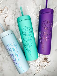 three different colored tumblers sitting next to each other on a marble surface with flowers painted on them