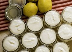 several jars filled with cream sitting next to lemons