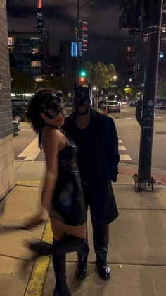 a man and woman dressed up in costumes standing on the side of a street at night