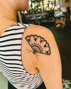 a woman with a fan tattoo on her left shoulder and right arm behind her back