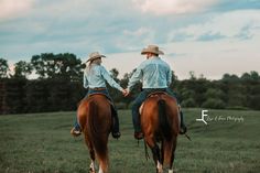 two people riding on the back of brown horses in a grassy field with trees behind them