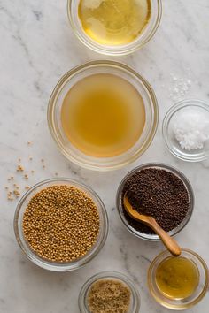 bowls filled with different types of food on top of a white marble countertop next to two wooden spoons