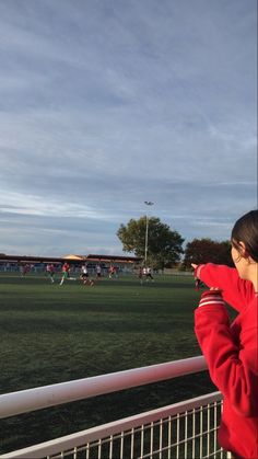 a girl in a red jacket looking out over a soccer field